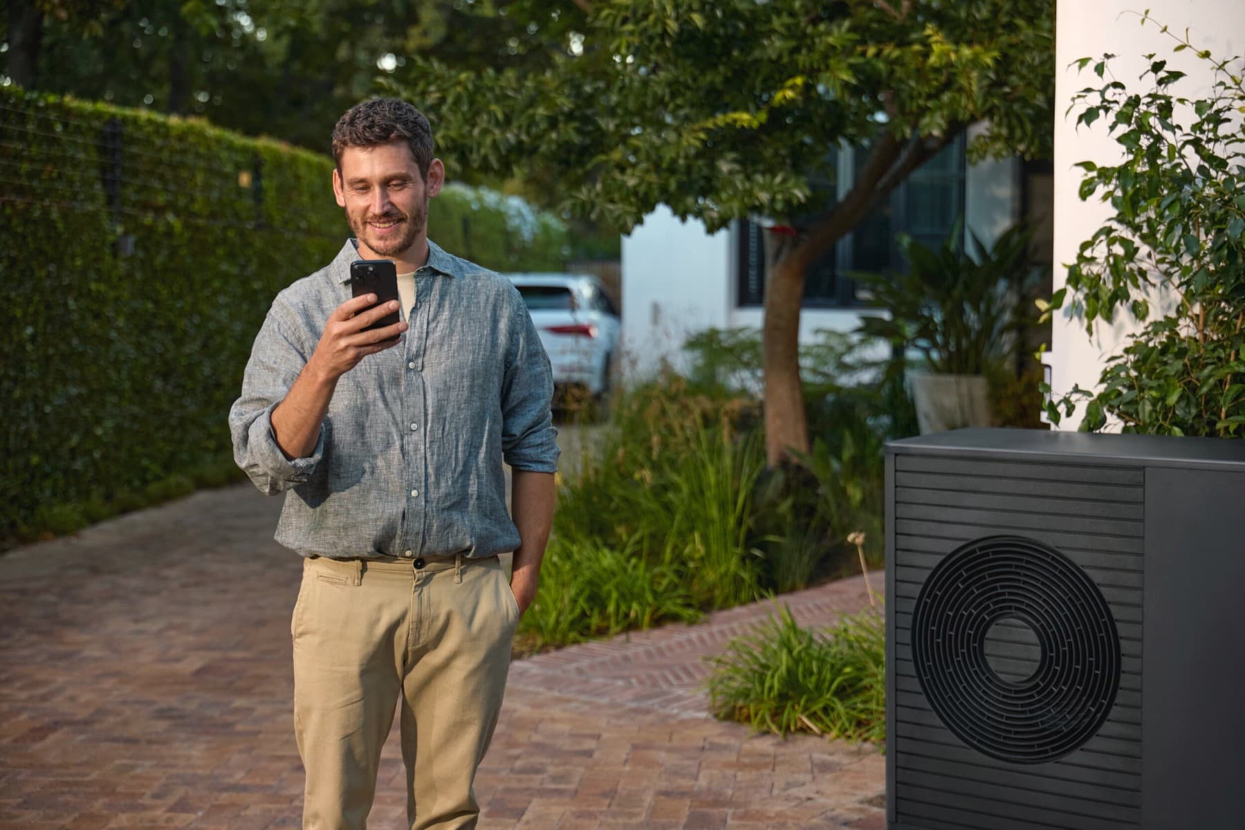 Man kijkt naar smartphone naast warmtepomp in tuin