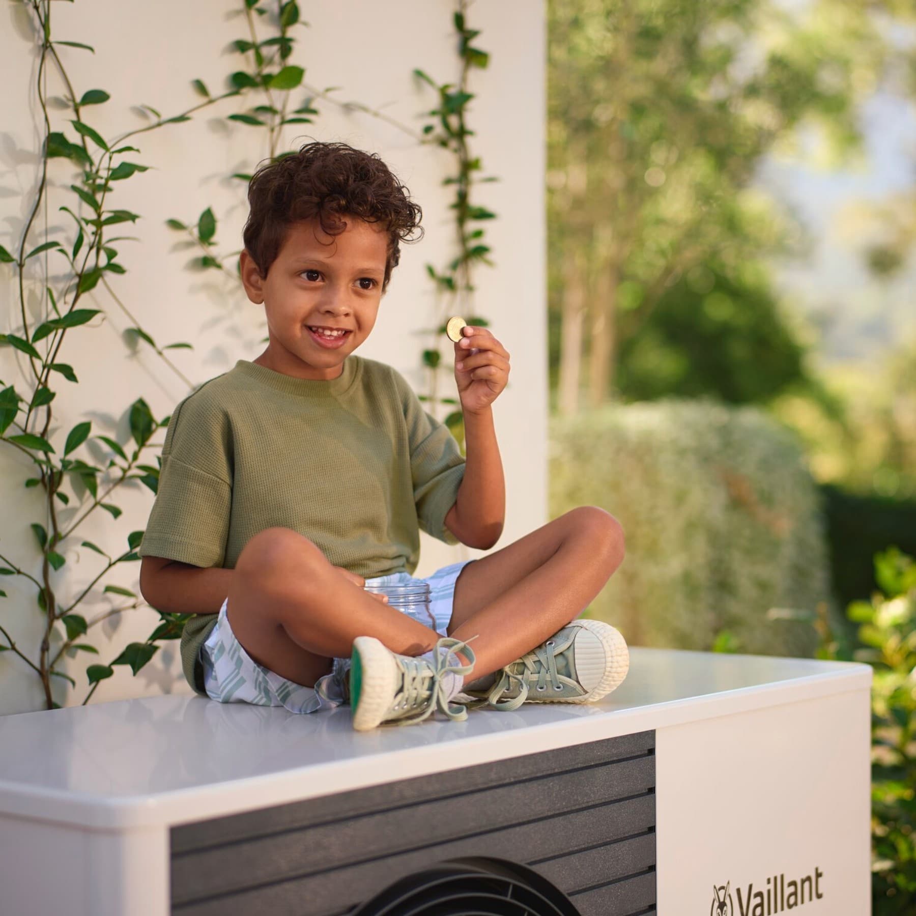 Een jongen met een muntje in zijn hand, zittend op een warmtepomp